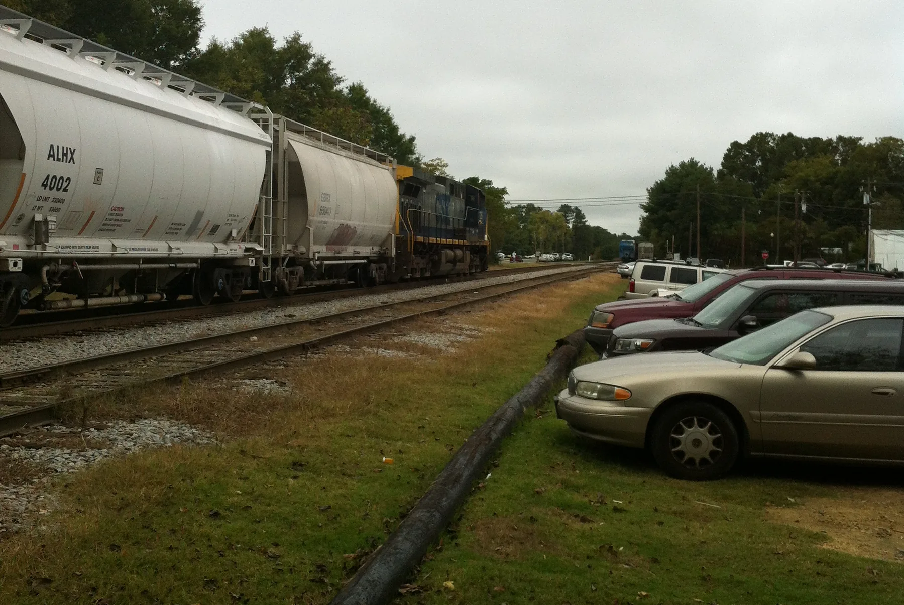 A CSX freight train passes the parking area beside the tracks next to the Apex Union Depot in downtown Apex