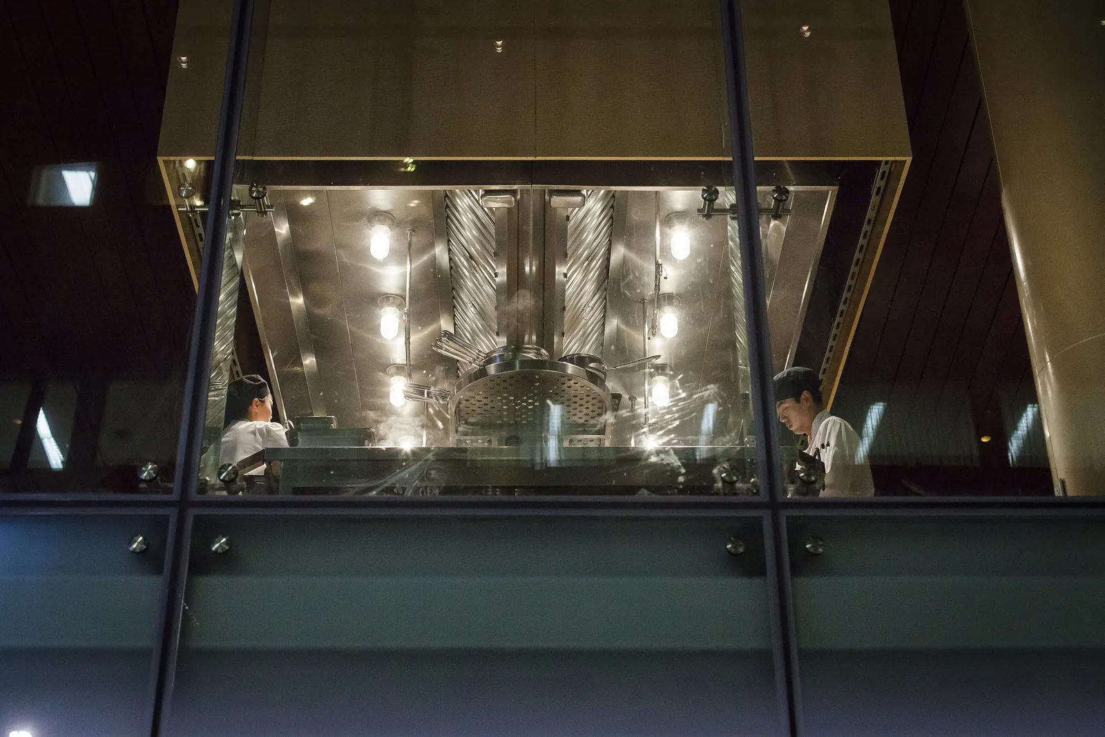 Cooks at work behind glass in a restaurant kitchen in New York City.