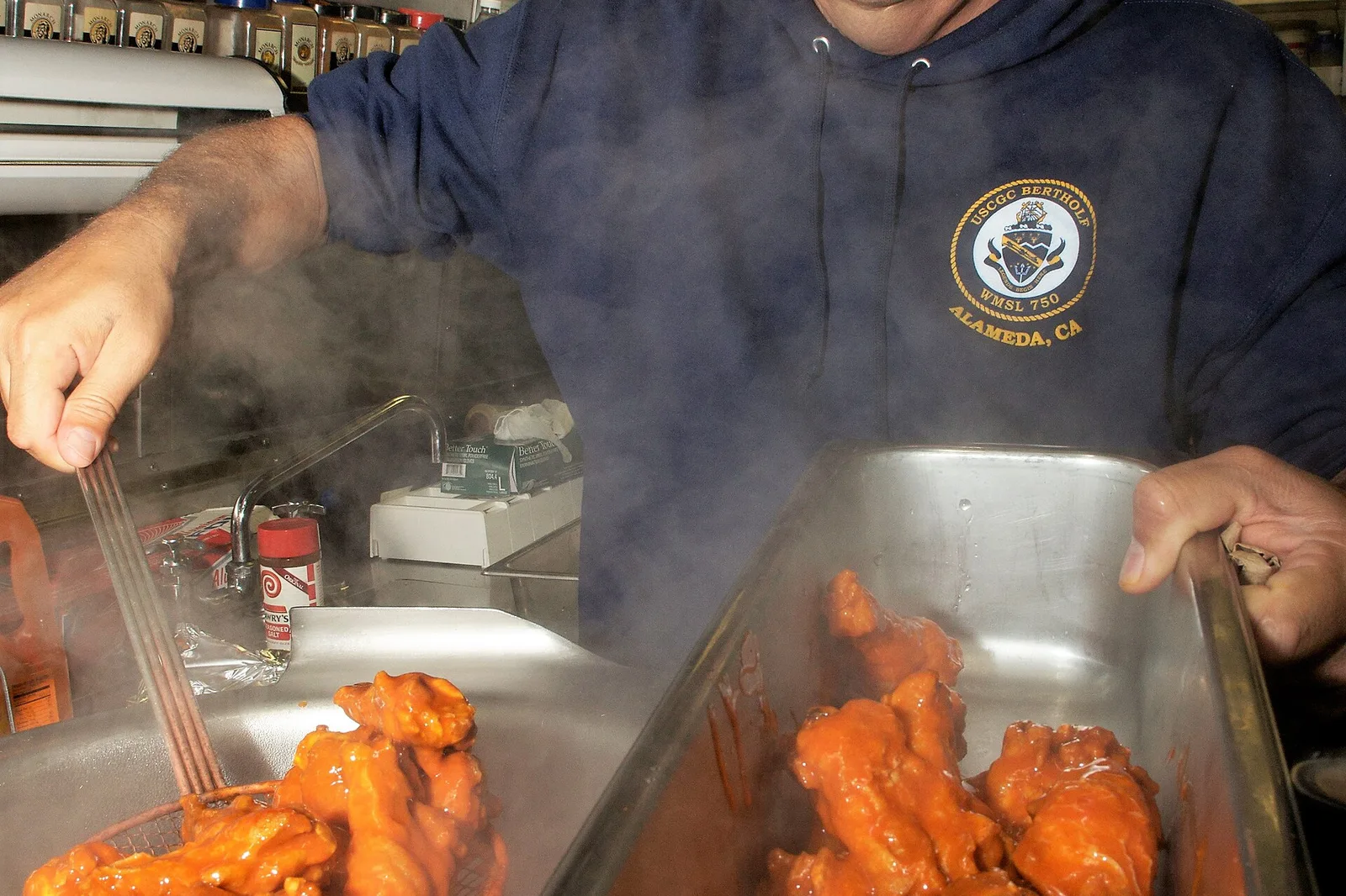A cook tosses buffalo chicken wings in sauce in a ship's galley. The photo was not taken in Apex.